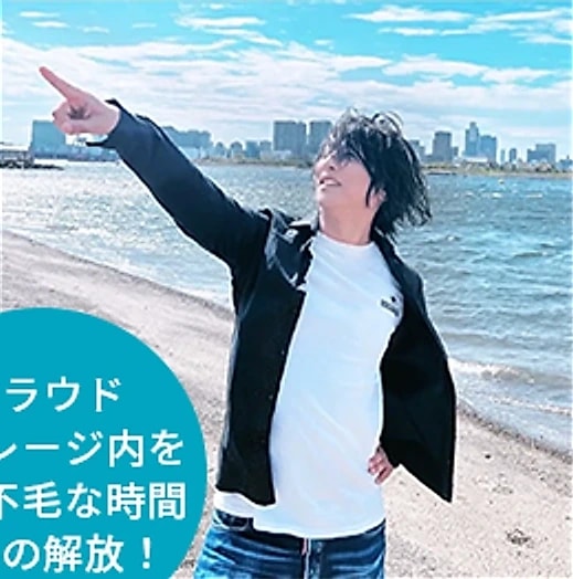 海辺で街並みを指さす草野哲也氏